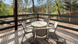 A covered outdoor seating area with a round table and four chairs, surrounded by a wooden deck and a wooden fence. - Rosella Views - Cosy Cottage at the Base of Mt Buller (Sawmill Settlement)