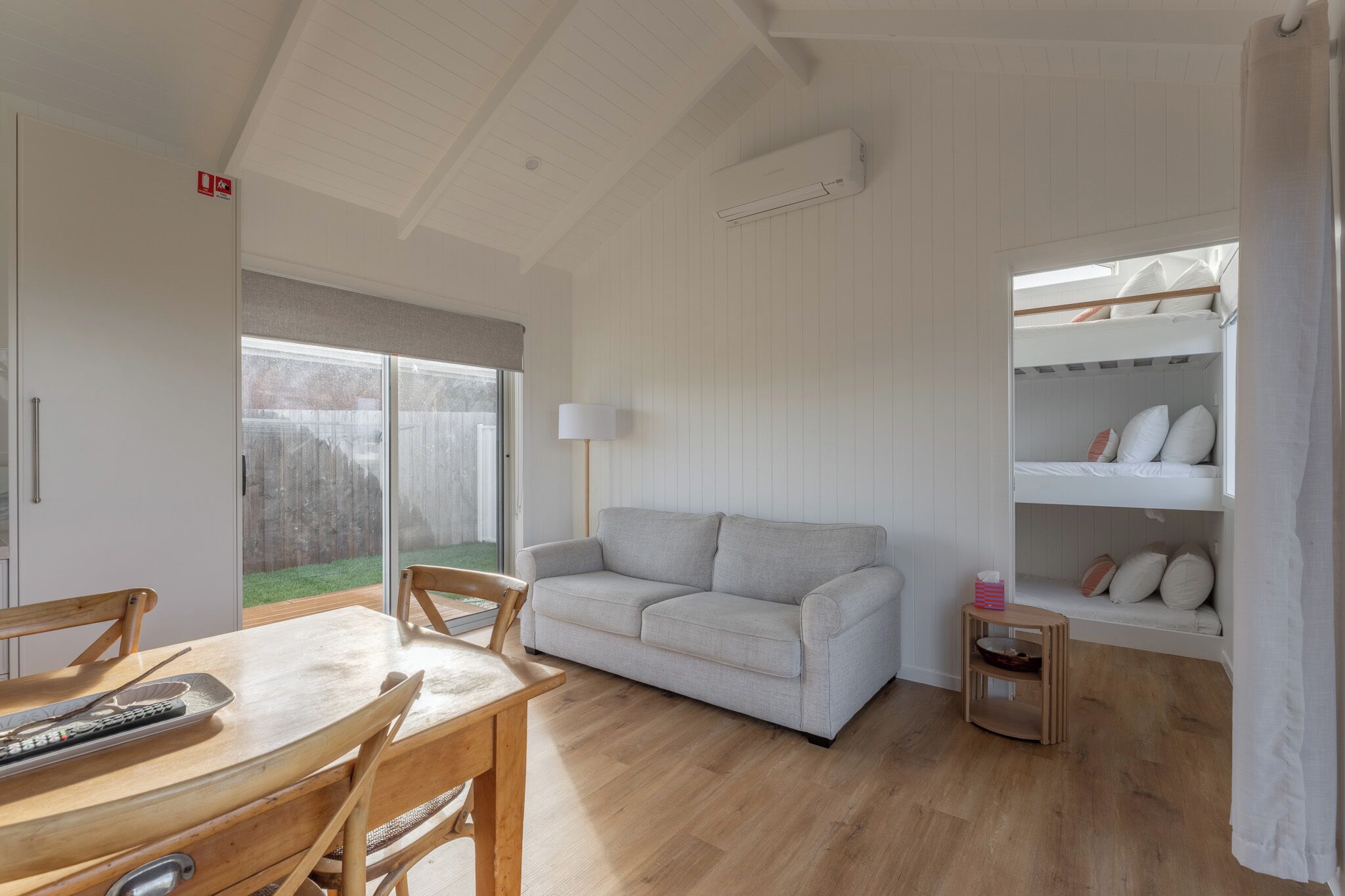 Una habitación con un sofá blanco, una mesa de comedor de madera y una litera con almohadas.