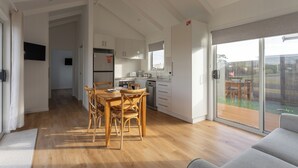 Ein geräumiger Wohnbereich mit einem Holzessttisch und Stühlen, einer Küche mit weißen Schränken und einer Glastür zum Balkon.