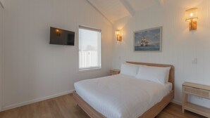 Ein Schlafzimmer mit einem Bett, einem an der Wand montierten Fernseher, einem Fenster und einem Gemälde.