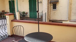 Un patio al aire libre con una mesa redonda y dos sillas, una sombrilla y una valla metálica.