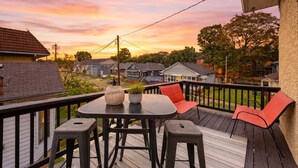 En terrass med ett bord och stolar, med utsikt över ett bostadsområde under solnedgången.