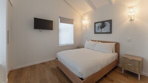 A bedroom with a wooden bed, a flat-screen TV mounted on the wall, a bedside table, and a nightstand.