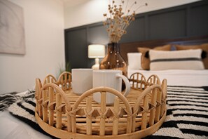 Una bandeja de madera ordenada con una taza blanca y un jarrón de flores secas sobre una cama con una manta a rayas.