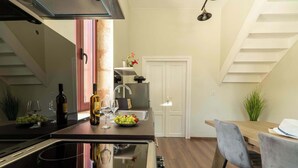 A modern kitchen with a central island, a dining area with a wooden table and chairs, and a staircase leading to an upper level. - Casa Chris (Chania)