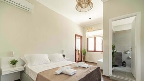 A modern bedroom with a large bed, bedside tables, a bedside plant, and a view of the bathroom. - Casa Chris (Chania)