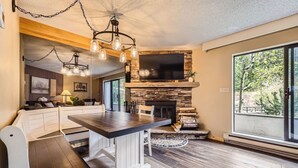 A modern kitchen with a stone fireplace, a dining area with a bench, and a large window offering a view of the outdoors. - Ski-In, Ski-Out From Studio, Ground Floor, Dog Friendly (Breckenridge)
