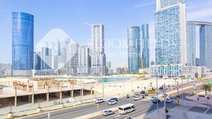 A cityscape with modern skyscrapers, a busy street with cars and a bus, and a waterfront area. - Bloomfields 1BR The Pearl of Julphar (Abu Dabi)