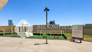 A playground area with a slide, swings, and a climbing structure. - Bloomfields 1BR The Pearl of Julphar (Abu Dabi)