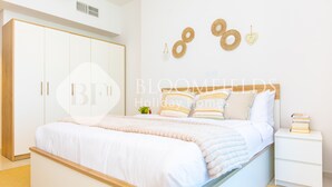 A bedroom with a large bed, a white wardrobe, and a bedside table with books. - Bloomfields 1BR The Pearl of Julphar (Abu Dabi)