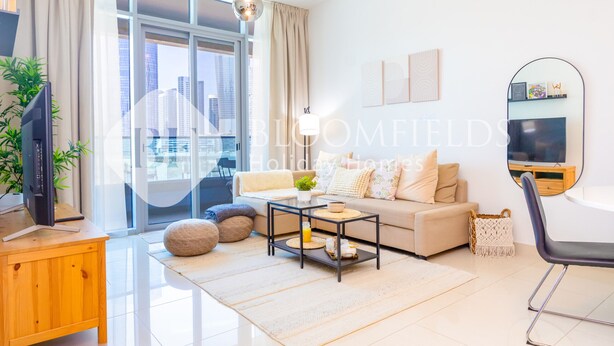 A modern living room with a sofa, coffee table, and TV. - Bloomfields 1BR The Pearl of Julphar (Abu Dabi)