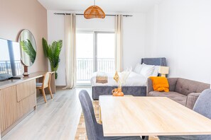 A modern hotel room with a bed, a sofa, a dining table, and a TV.