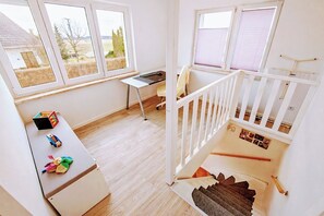 Ein Zimmer mit Schreibtisch, Stuhl, einem kleinen Tisch mit Spielzeug, einer Treppe und einem Fenster mit Jalousien.