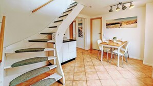 A modern kitchen with white cabinets, a dining area with a table and chairs, and a spiral staircase with green steps.