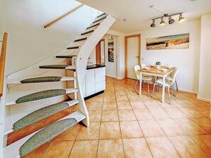 Eine moderne Küche mit weißen Schränken, ein Essbereich mit Tisch und Stühlen sowie eine Wendeltreppe mit grünen Stufen.