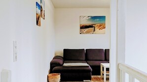 A hallway with a wooden floor, a dark-colored sofa, a small table, and a painting on the wall.