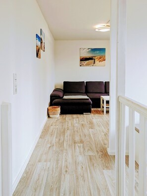 Ein Flur mit Holzboden, einem dunkelgrauen Sofa, einem kleinen Tisch und einem Gemälde an der Wand.