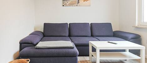 A living room with a sectional sofa, a white coffee table, a woven basket, and a painting of a beach scene.