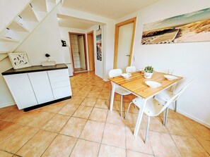 Una cocina con armarios blancos, una mesa de comedor de madera con sillas blancas y un piso de baldosas.