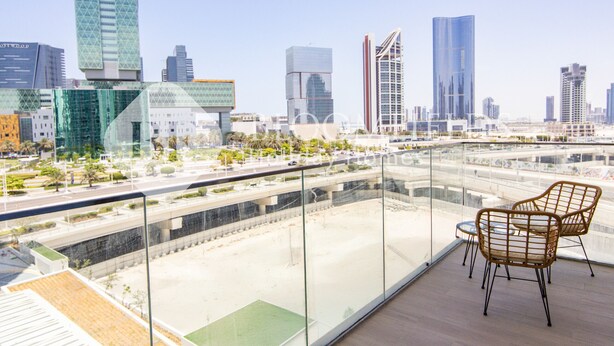 Een hoog gebouw met een glazen balkon, met twee rieten stoelen en uitzicht op een stadsgezicht met moderne wolkenkrabbers.