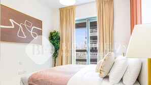 Un dormitorio con cama, mesita de noche, planta y ventana con cortinas.
