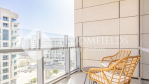 A balcony with a view of a cityscape, two wicker chairs, and a tiled wall.
