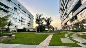 A modern building with a courtyard featuring a lawn, palm trees, and a checkered pathway.
