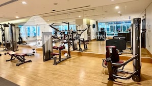 A spacious gym with various exercise machines, a large mirror, and a wooden floor.