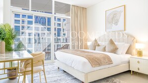 A modern bedroom with a large bed, a dining table, and a view of a building through large windows.