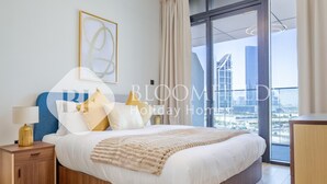 Een moderne hotelkamer met een groot bed, een nachtkastje, een lamp en uitzicht op de stad door grote ramen.