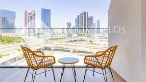 Een balkon met twee rieten stoelen en een kleine ronde tafel, met uitzicht op een stadsgezicht met moderne gebouwen en een snelweg.