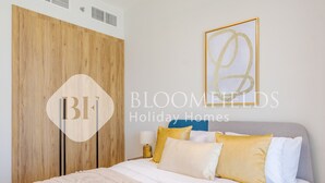 Een slaapkamer met een houten garderobe, een bed met wit beddengoed en meerdere kussens, plus een abstract kunstwerk aan de muur.