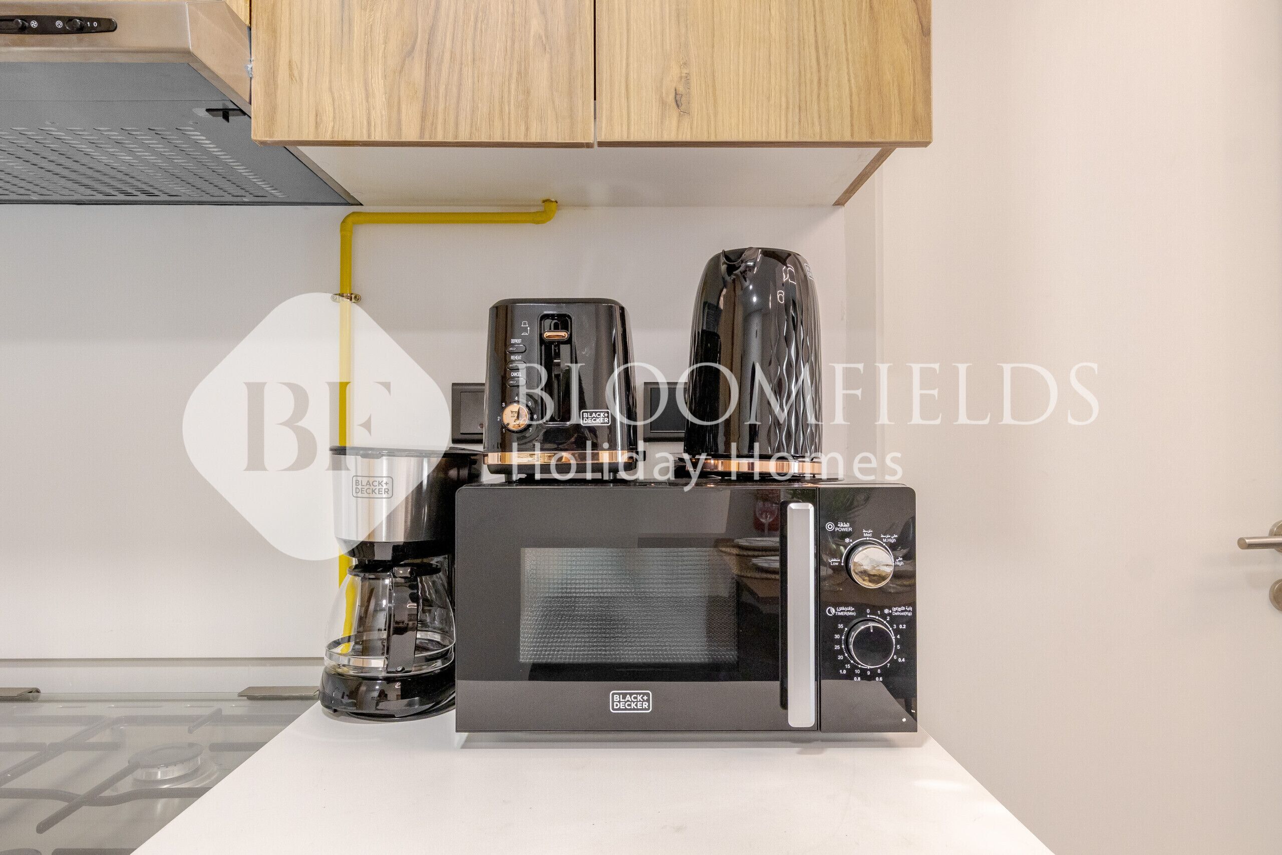 Een keuken met een magnetron, koffiezetapparaat en een koffiekan op het aanrecht.