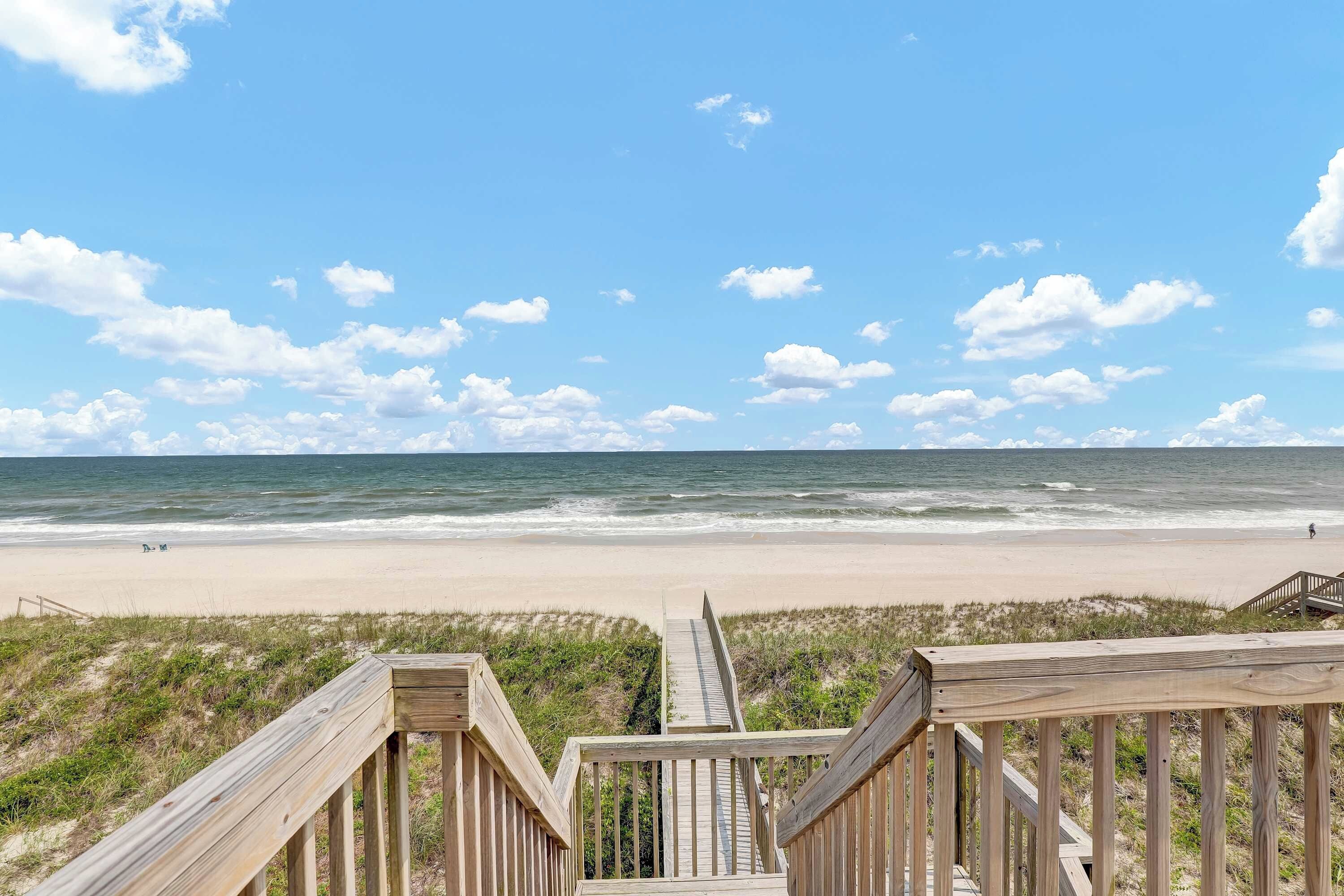 A wooden boardwalk leading to a beach with a clear view of the ocean and sky.