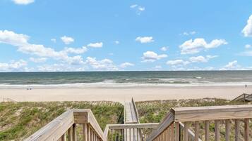 A wooden boardwalk leading to a beach with a clear view of the ocean and sky.