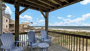 A wooden deck with two Adirondack chairs and a small table, overlooking a beach with a clear sky.