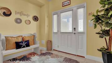 A hallway with a white bench, a welcome sign, decorative plates, and a door with blinds.