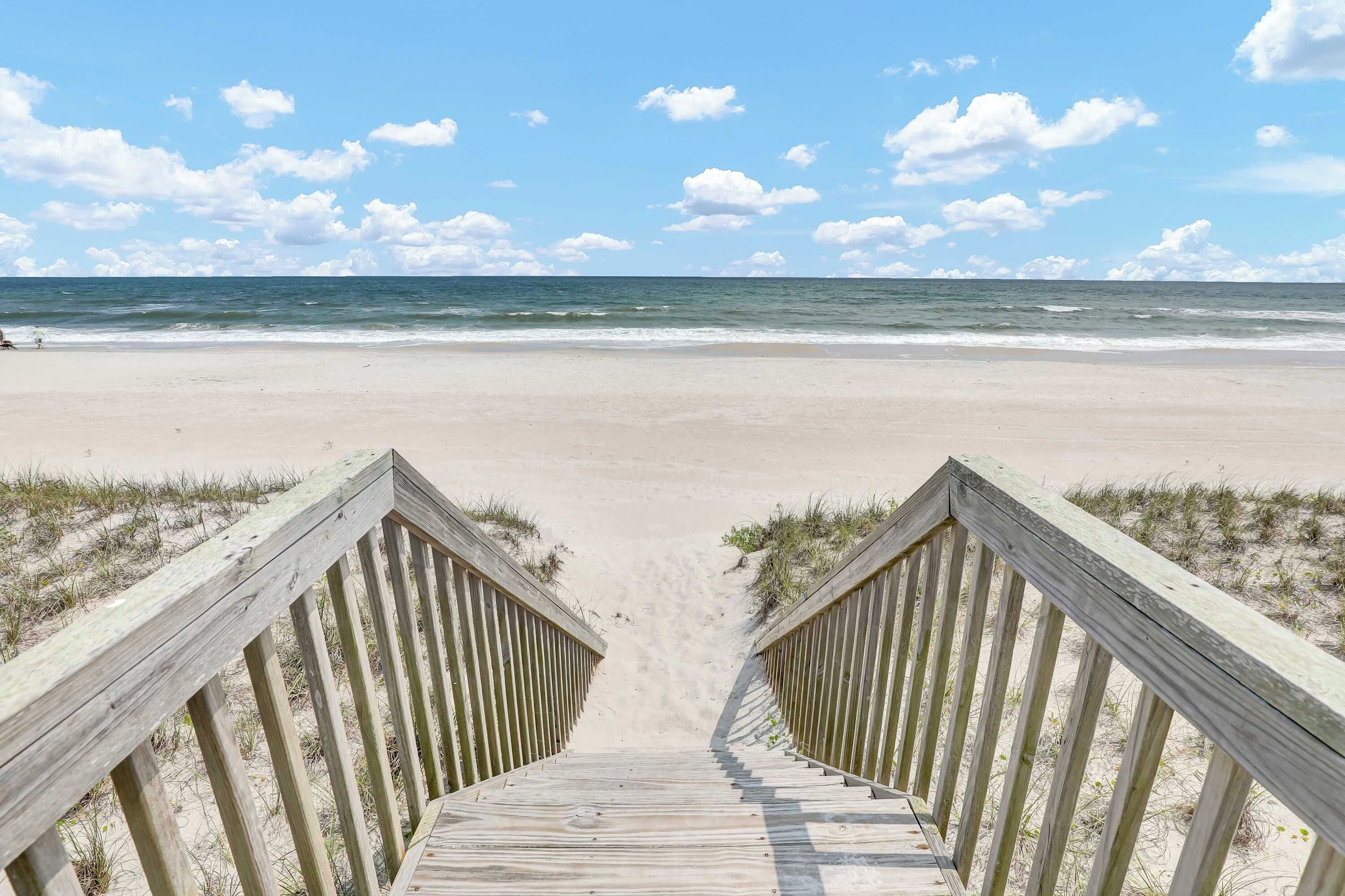 A wooden boardwalk leading to a beach with a clear sky and ocean view.
