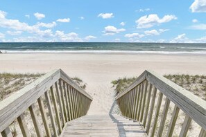 A wooden boardwalk leading to a beach with a clear sky and ocean view.