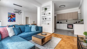 A modern living room with a blue sofa, a wooden coffee table, and a kitchen in the background. - Cozyopolis - Timeless 3-BR in Athens  (Athens)
