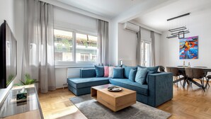 A modern living room with a sectional sofa, a coffee table, a dining area with chairs, and a painting on the wall. - Cozyopolis - Timeless 3-BR in Athens  (Athens)