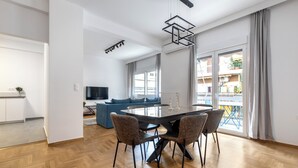 A modern living room with a dining table, chairs, and a sofa. There is a TV and a balcony visible through the window. - Cozyopolis - Timeless 3-BR in Athens  (Athens)