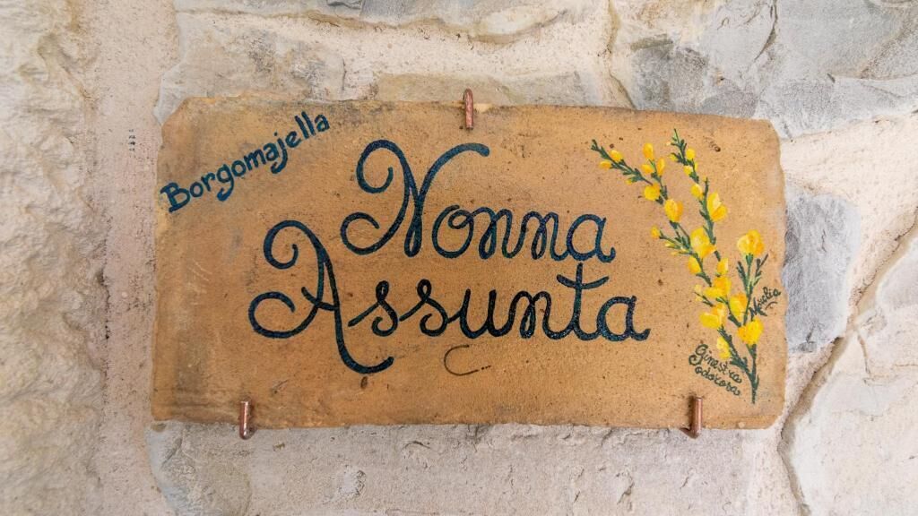 Une enseigne portant l’inscription « Borgomajella Nonna Assunta » et ornée d’un motif floral décoratif.