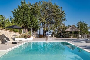 Une piscine équipée de chaises longues, de parasols et bordée d’un mur en pierre.
