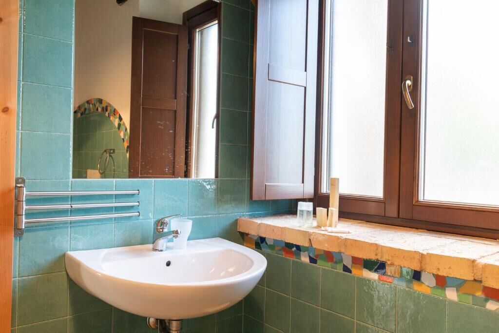 Casa de banho com uma pia branca, um espelho e uma janela.