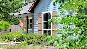 Une maison bleue avec un porche en bois, un drapeau et un jardin.