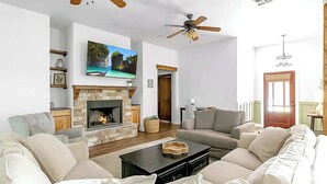 Un salon avec une cheminée, des canapés, un téléviseur et des ventilateurs de plafond.
