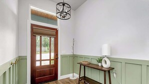 Un couloir avec un plancher en bois, une porte en bois dotée d’une fenêtre, des lambris verts, une table avec une lampe et un lampadaire.