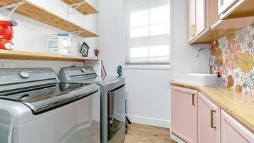 Een kleine keuken met roestvrijstalen apparatuur, houten planken en een raam met zonwering.