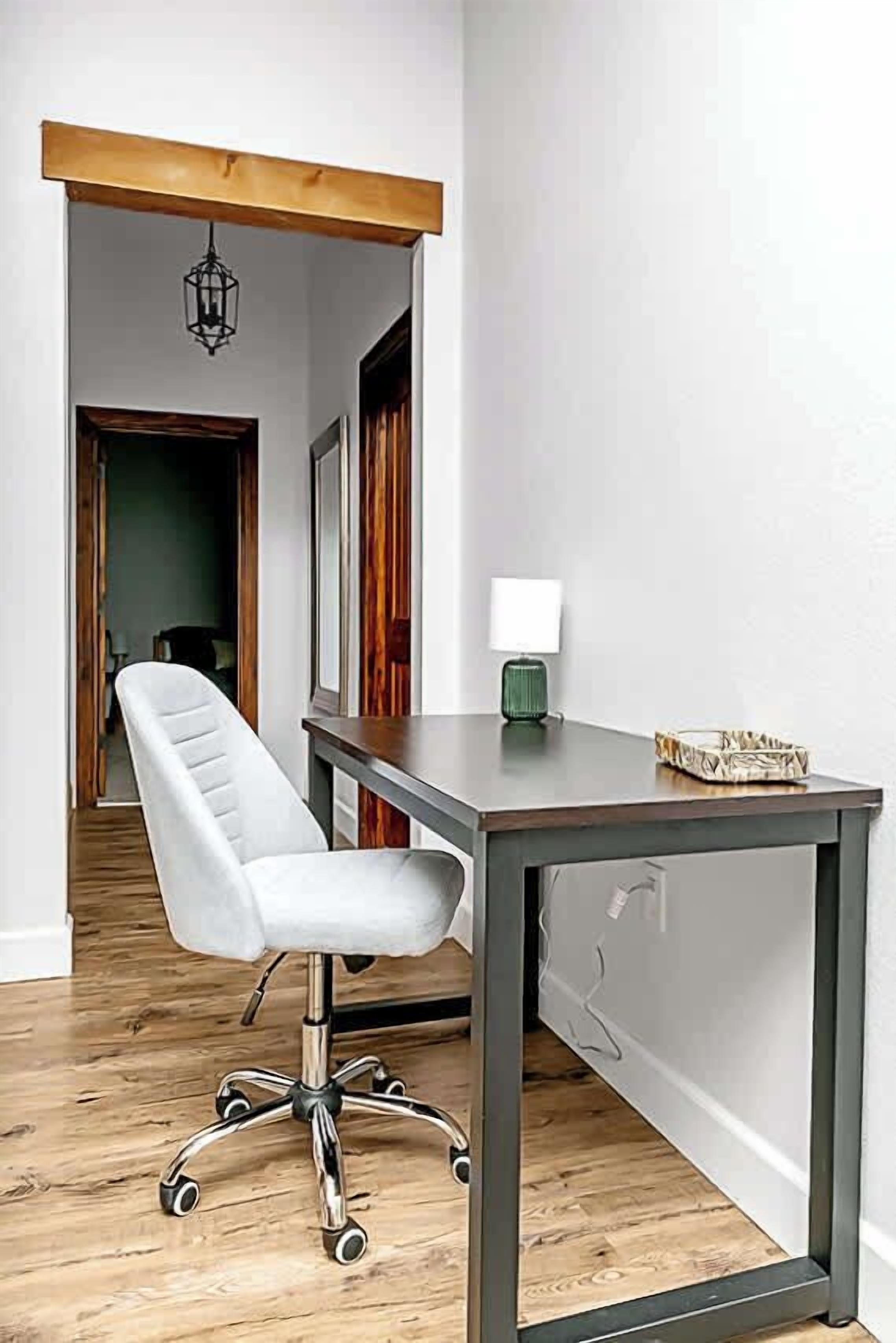 A modern office space with a white office chair, a dark wooden desk, and a green floor lamp.